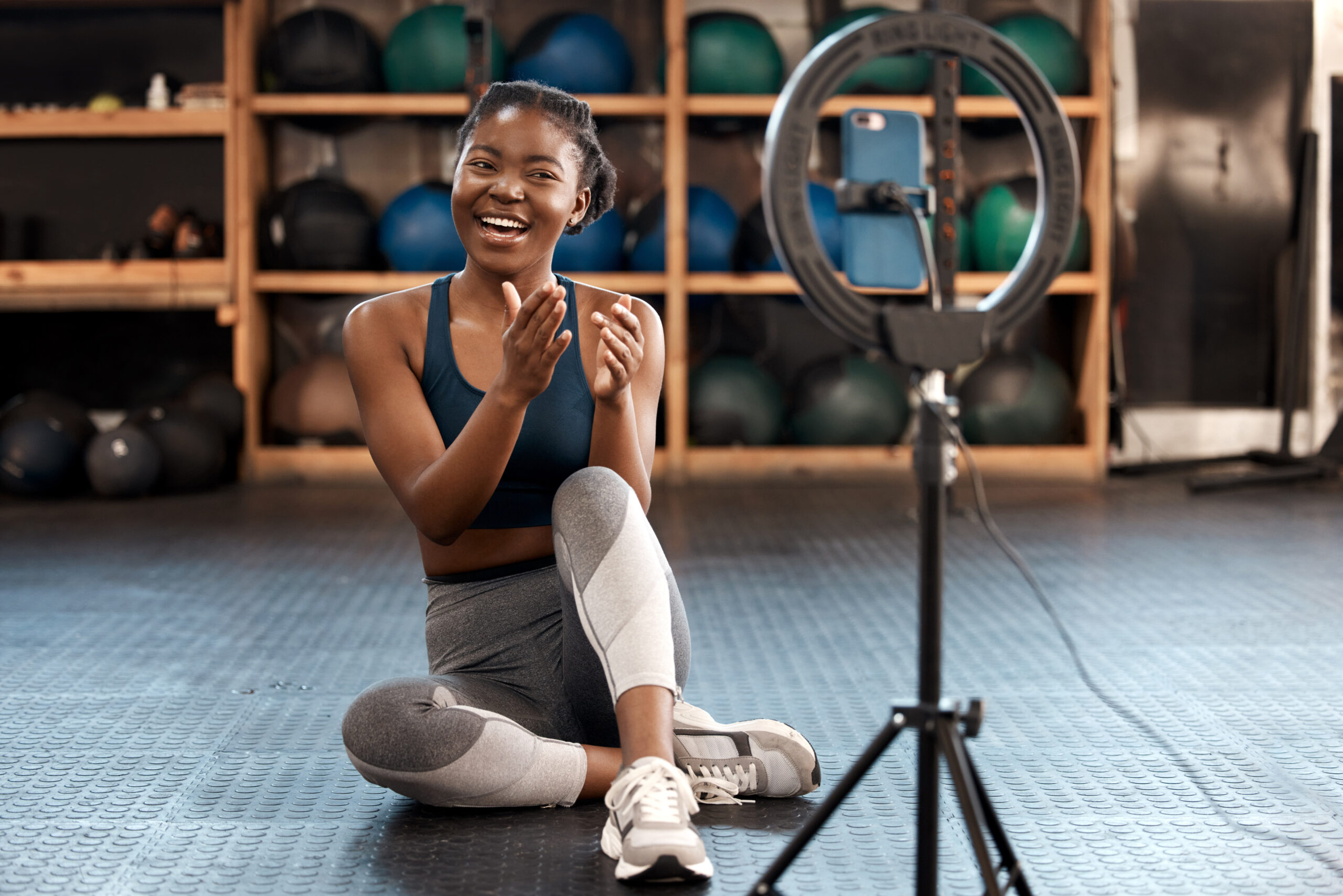 A Black woman fitness influencer live streams at the gym, helping her audience train.